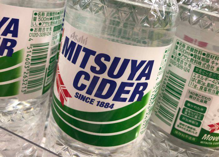 Mitsuya Cider lined up in a fridge at a supermarket.